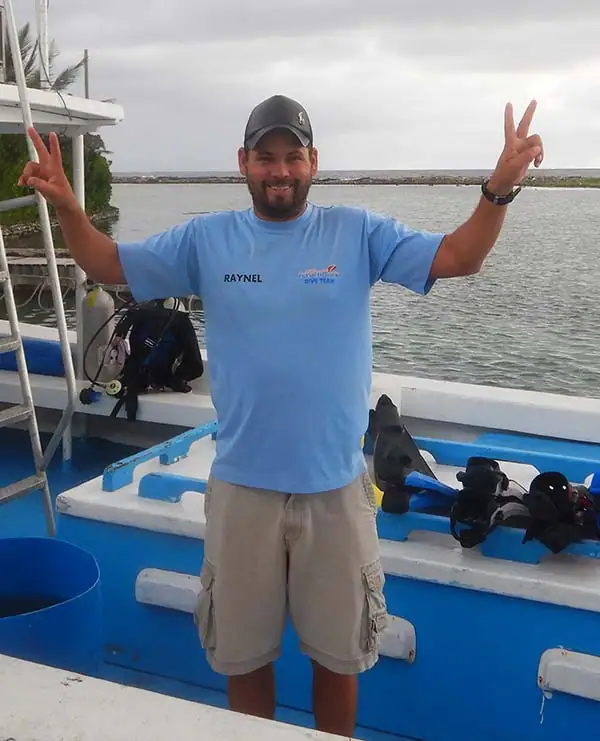 Happy staff member on boat at Dunbar Rock, smiling and making peace signs, with water and boat equipment in background.